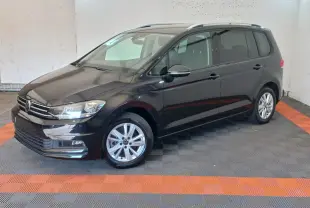 Volkswagen Touran noir vu en 3/4 avant droit, avec jantes alliage et barres de toit chromées visibles.