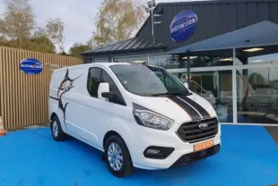 Ford Transit Custom blanc glacier en 3/4 avant droit avec bandes noires sur le capot et marquage poisson sur la porte.