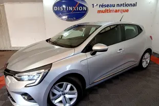 Vue 3/4 avant droite d'une Renault Clio gris clair avec feux LED allumés dans un showroom intérieur.