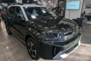 Vue 3/4 avant gauche d'un Citroën C3 Aircross 2025 vert Montana avec toit blanc en showroom lumineux.