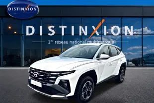 Vue 3/4 avant droite du Hyundai Tucson blanc 2026 avec calandre noire et jantes alliage 17 pouces devant un showroom Distinxion.