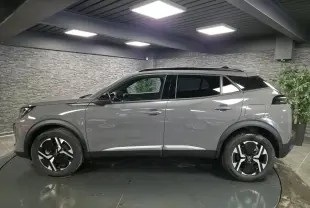 Vue de profil côté gauche d'un Peugeot 2008 gris métallisé avec jantes alliage bi-ton noir et toit noir dans un intérieur showroom.