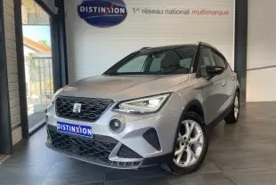 Vue 3/4 avant droite d'une SEAT Arona 2024 gris clair GRS avec jantes alliage et calandre noire en showroom.