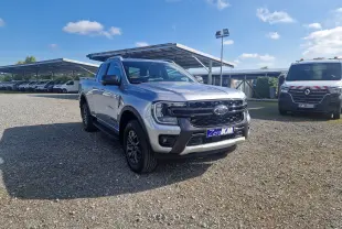 Ford Ranger Super Cabine gris Iconic vu en 3/4 avant droit sur un parking extérieur sous un ciel bleu.