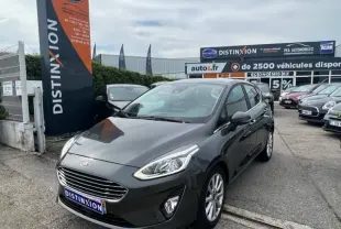 Ford Fiesta 2018 gris vue 3/4 avant droit sur parking avec panneau Distinxion en arrière-plan