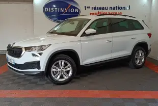 Vue de profil droit d'un Skoda Kodiaq blanc 2022 dans un showroom, avec jantes alliage et barres de toit noires.