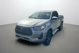 Toyota Hilux 4x4 gris acier en 3/4 avant droit, avec calandre chromée et jantes foncées visibles.