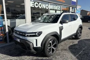 SUV Dacia Duster blanc métallisé en 3/4 avant droit, avec barres de toit noires et jantes alliage 18 pouces.