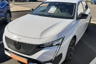 Peugeot 308 blanc vue 3/4 avant droit, avec calandre noire distinctive et feux LED verticaux allumés.
