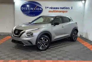 Nissan Juke gris clair vu en 3/4 avant droit, avec jantes alliage noires et calandre V-Motion chromée.