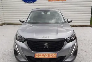 Peugeot 2008 gris Artense vue 3/4 avant droit, avec calandre noire et phares LED, stationnée devant un mur blanc.