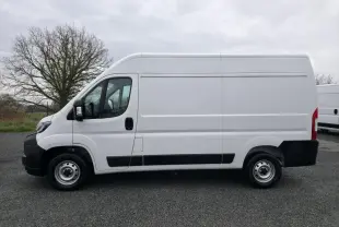 Peugeot Boxer Fourgon blanc en vue de profil côté gauche sur un sol goudronné, fond d'arbre et ciel nuageux.