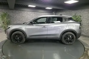 Vue de profil côté gauche d'une Alfa Romeo Junior 1.2 Ibrida gris métallisé avec jantes alliage noires dans un showroom.