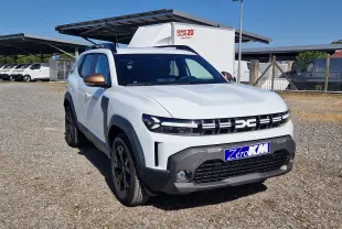 Vue 3/4 avant gauche d'un Dacia Duster blanc 2026 avec rétroviseurs bronze et calandre distinctive noire.