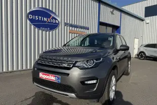 Vue 3/4 avant d'un Land Rover Discovery Sport gris métallisé garé devant un bâtiment commercial.