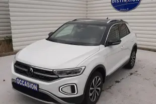 Volkswagen T-Roc blanc pur avec toit noir, vue 3/4 avant droit, stationné devant un mur blanc avec panneau Distinxion.
