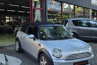 MINI Cabriolet grise vue 3/4 avant droit, capote noire fermée, stationnée devant un garage automobile.