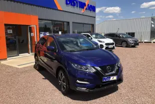 Nissan Qashqai bleu métallisé en 3/4 avant droit, stationné devant un concessionnaire avec panneau Distinxion visible.