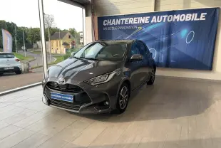 Toyota Yaris Hybride 116h Design gris foncé vue 3/4 avant en showroom avec éclairage naturel et bannière bleue.