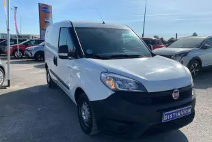 Fiat Doblo blanc vu en 3/4 avant droit, fourgon tôlé avec pare-chocs noirs et porte latérale droite visible.