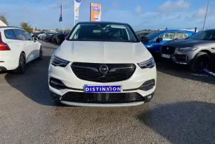 Vue frontale d'un Opel Grandland blanc nacré avec toit noir, calandre noire et plaque Distinxion visible.