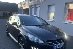 Peugeot 508 SW Hybrid4 gris vue 3/4 avant droit, feux LED allumés, jantes aluminium et barres de toit visibles.