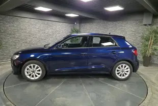 Profil côté gauche d'une Audi A1 Sportback 2024 bleu métallisé avec jantes aluminium 16 pouces dans un showroom.