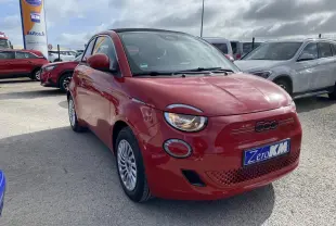 Fiat 500 Cabriolet électrique rouge vue 3/4 avant droit avec phares allumés sur parking extérieur.