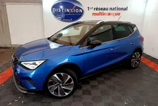 SEAT Arona bleu en 3/4 avant droit, toit noir et jantes alliage distinctives dans un showroom intérieur.