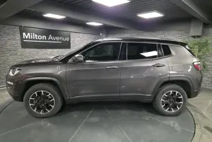 Profil côté gauche d'un Jeep Compass gris foncé avec jantes alliage noires et toit noir en showroom.