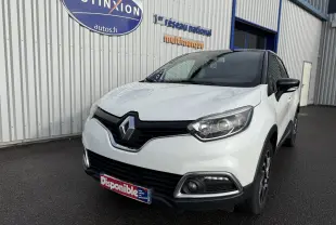 Renault Captur blanc en 3/4 avant droit, avec calandre noire et feux LED, stationné devant un bâtiment industriel.