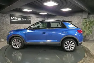 Vue de profil côté gauche d'un Volkswagen T-Roc bleu foncé avec jantes alliage et toit noir en intérieur showroom.