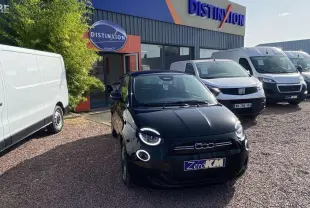 Vue avant d'une Fiat 500 électrique noire métal stationnée devant un concessionnaire avec d'autres véhicules blancs.