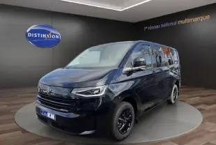 Vue 3/4 avant droit d'un Volkswagen Transporter noir 2026 avec jantes noires et phares LED dans un showroom.