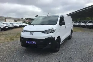 Vue 3/4 avant d’un FIAT Scudo Fourgon blanc 2024 avec pare-chocs noir et plaque de protection, stationné sur un sol gravillonné.