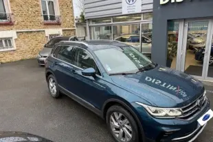 Volkswagen Tiguan 2022 bleu nuit en 3/4 avant droit devant un concessionnaire avec toit panoramique et jantes alliage.