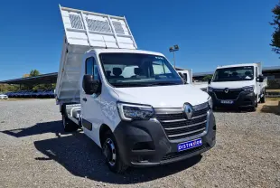 Renault Master Benne blanc vue 3/4 avant droit avec benne relevée et roues jumelées sur sol gravillonné.