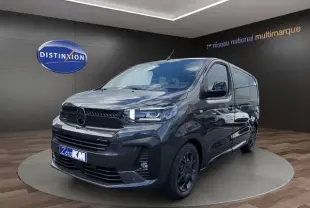 Vue 3/4 avant d'un Citroën Jumpy gris foncé, avec calandre noire et jantes sombres, en intérieur showroom.