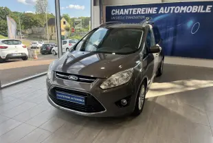 Ford Grand C-Max marron en 3/4 avant droit, exposée en showroom avec éclairage naturel et panneau publicitaire en arrière-plan