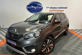 Vue 3/4 avant d'un Peugeot 5008 gris métallisé, avec jantes alliage et feux allumés en showroom.
