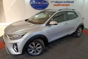 Vue 3/4 avant droit d'un KIA STONIC 1.0 T-GDI 100 Urban gris clair stationné en intérieur sur sol carrelé.