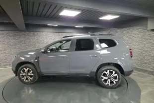 Vue de profil côté gauche d'un Dacia Duster 2024 gris urbain avec jantes alliage 17 pouces et barres de toit.