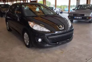 Peugeot 207+ noire vue 3/4 avant droit dans un garage, mettant en valeur ses phares et calandre distinctifs.