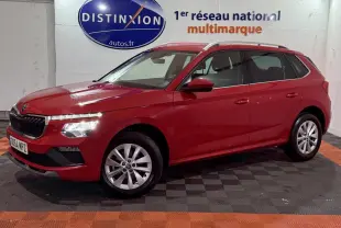 Vue 3/4 avant gauche d'un Skoda Kamiq rouge 2024 avec jantes alliage et rails de toit noirs en intérieur showroom.