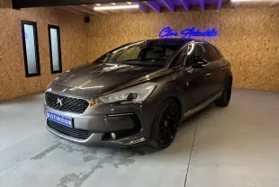 DS5 gris 3/4 avant droit en intérieur, avec jantes noires et calandre distinctive DS sous néon bleu.