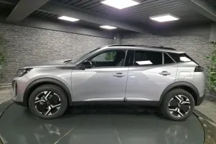Vue latérale droite d'un Peugeot 2008 gris métallisé avec jantes bi-ton et toit noir en intérieur showroom.
