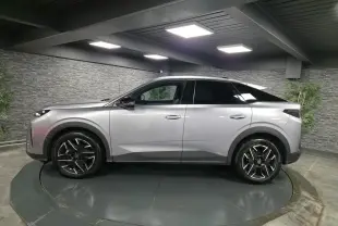 Vue de profil côté gauche d’un Peugeot 3008 gris métallisé 2025 avec jantes alliage noires et toit noir dans un showroom.