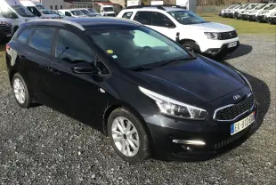 KIA CEE'D SW noire vue en 3/4 avant droit sur un parking, avec jantes alliage et feux allumés.