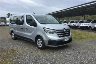 Renault Trafic Combi gris clair métal vu en 3/4 avant droit sur un parking avec plusieurs véhicules blancs en arrière-plan.