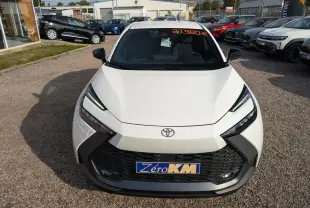 Vue avant d'un Toyota C-HR blanc 2024 hybride, avec calandre noire et phares LED fins, en concession extérieure.